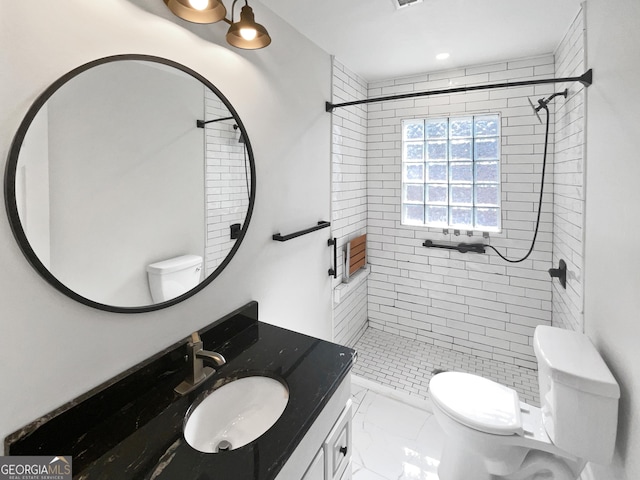 bathroom with tiled shower, vanity, and toilet