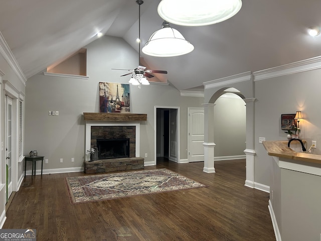 unfurnished living room with ceiling fan, vaulted ceiling, crown molding, a stone fireplace, and decorative columns