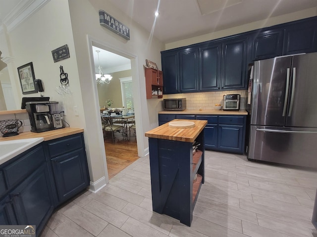 kitchen with butcher block counters, stainless steel fridge, tasteful backsplash, blue cabinets, and ornamental molding