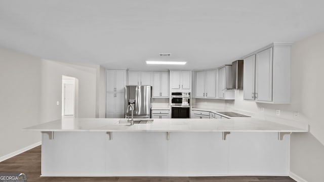 kitchen featuring wall chimney exhaust hood, stainless steel appliances, a breakfast bar, and kitchen peninsula