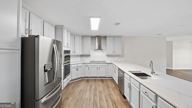 kitchen with sink, white cabinets, light stone counters, appliances with stainless steel finishes, and wall chimney range hood