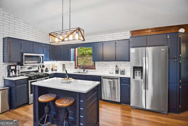 kitchen with appliances with stainless steel finishes, hanging light fixtures, vaulted ceiling, a kitchen island, and sink