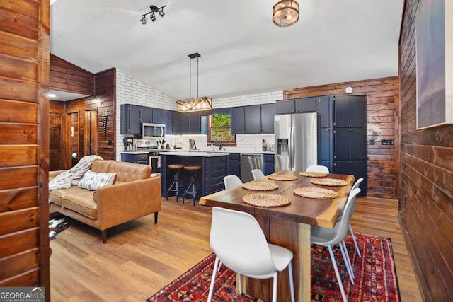 dining area featuring light wood-type flooring, lofted ceiling, and wooden walls