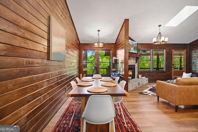 dining room with a fireplace, light hardwood / wood-style flooring, lofted ceiling with skylight, and wooden walls