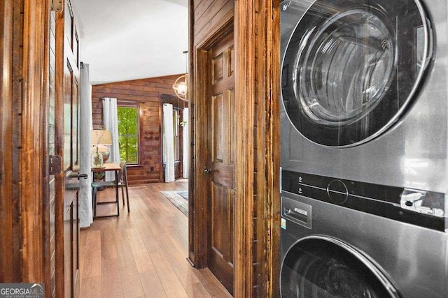 laundry room featuring stacked washer / drying machine, wood walls, and light hardwood / wood-style flooring