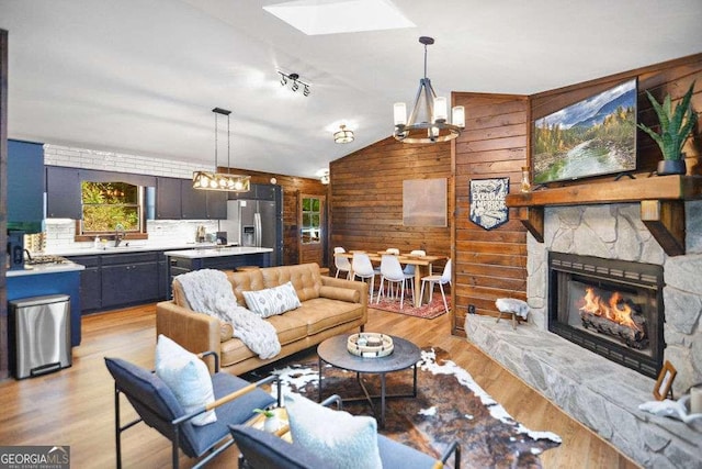 living room featuring a stone fireplace, light wood-type flooring, lofted ceiling, a chandelier, and sink