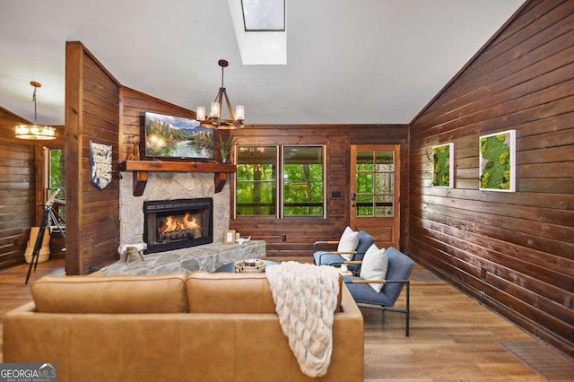 living room featuring vaulted ceiling with skylight, a notable chandelier, and wooden walls