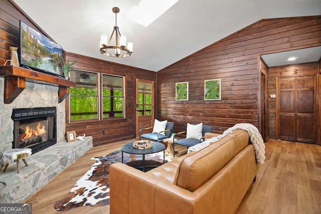 living room featuring vaulted ceiling, a fireplace, an inviting chandelier, wooden walls, and light hardwood / wood-style flooring