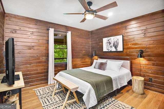 bedroom featuring ceiling fan, light hardwood / wood-style flooring, and wooden walls