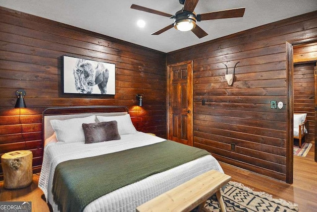 bedroom with ceiling fan, hardwood / wood-style flooring, and wooden walls