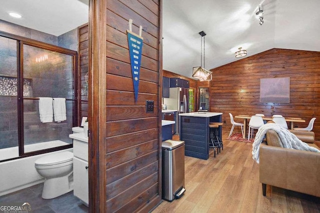 full bathroom featuring lofted ceiling, vanity, wooden walls, toilet, and combined bath / shower with glass door