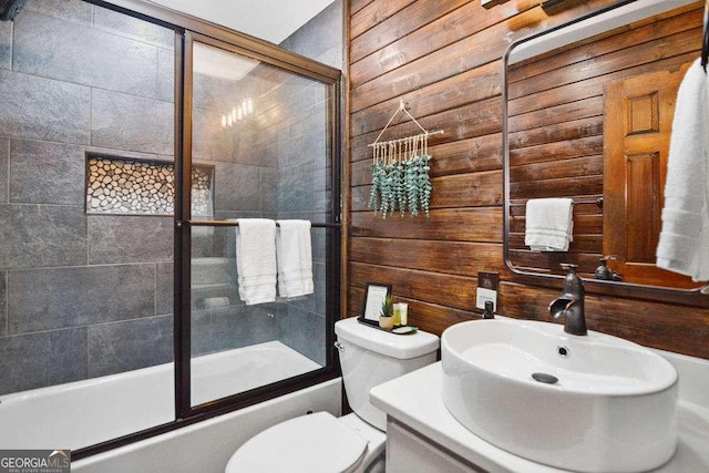 full bathroom featuring bath / shower combo with glass door, toilet, vanity, and wood walls