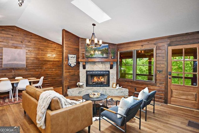 living room with vaulted ceiling with skylight, wood-type flooring, a fireplace, wood walls, and a chandelier