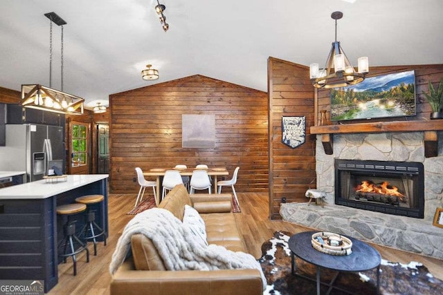 living room with light hardwood / wood-style floors, wood walls, lofted ceiling, and a stone fireplace