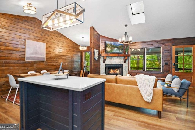 living room featuring vaulted ceiling, a fireplace, a notable chandelier, wood walls, and light hardwood / wood-style floors