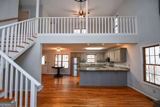 kitchen with kitchen peninsula, stainless steel fridge, gray cabinetry, dark hardwood / wood-style floors, and a towering ceiling