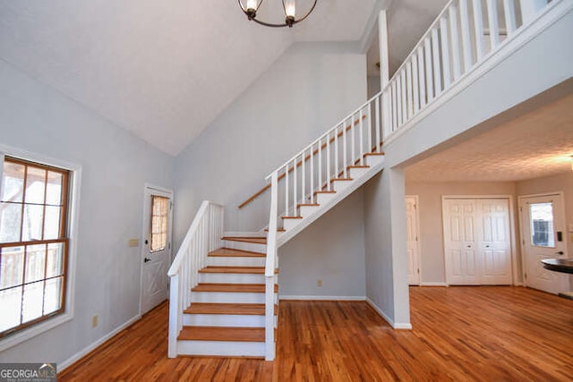 stairs featuring hardwood / wood-style flooring, plenty of natural light, high vaulted ceiling, and a notable chandelier