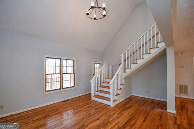 stairway with hardwood / wood-style flooring, high vaulted ceiling, and a chandelier