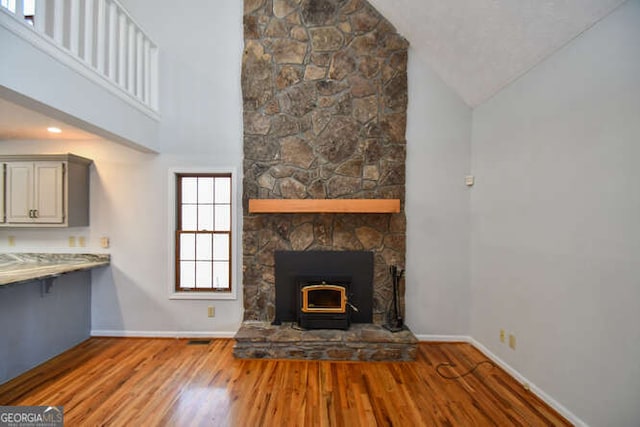 unfurnished living room with high vaulted ceiling, a wood stove, and wood-type flooring