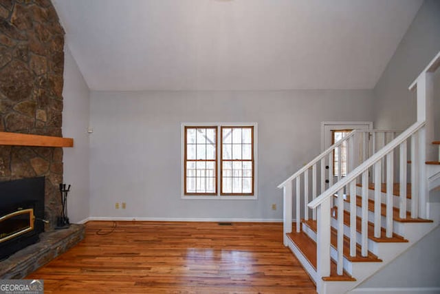 living room with hardwood / wood-style floors, lofted ceiling, and a stone fireplace