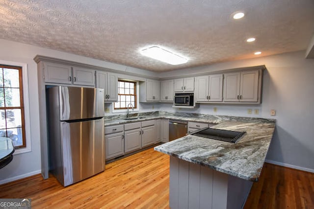 kitchen featuring kitchen peninsula, sink, appliances with stainless steel finishes, a textured ceiling, and light stone counters