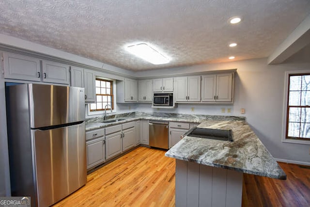 kitchen with kitchen peninsula, appliances with stainless steel finishes, a textured ceiling, light stone counters, and sink