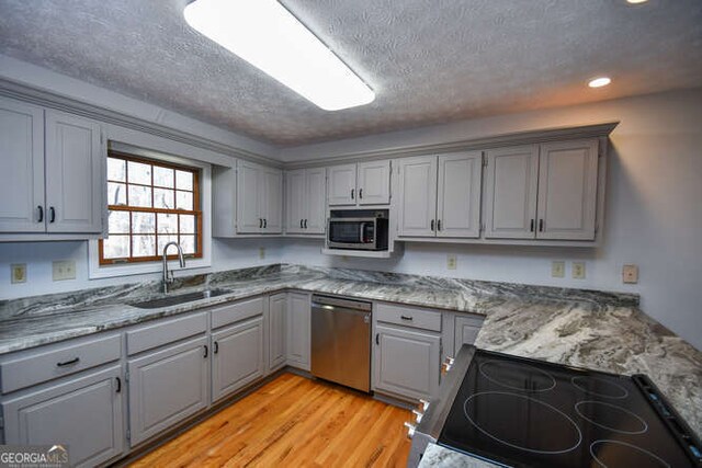 kitchen with a textured ceiling, gray cabinets, appliances with stainless steel finishes, and sink