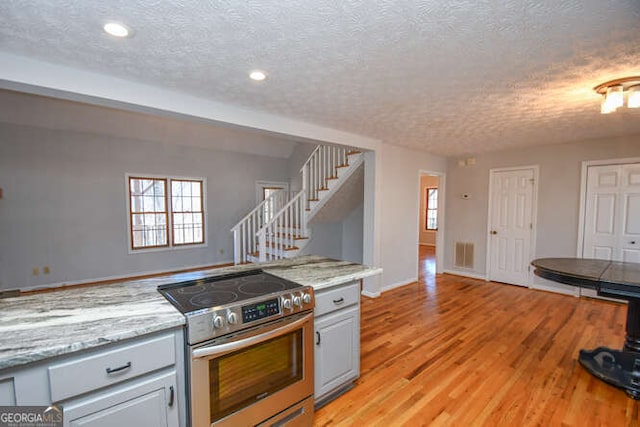 kitchen with electric stove, light stone countertops, a textured ceiling, and light hardwood / wood-style floors