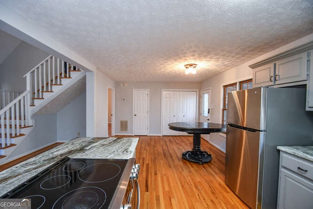 kitchen with light hardwood / wood-style floors, appliances with stainless steel finishes, gray cabinetry, a textured ceiling, and light stone counters