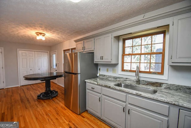 kitchen featuring gray cabinets, sink, stainless steel refrigerator, light wood-type flooring, and a textured ceiling