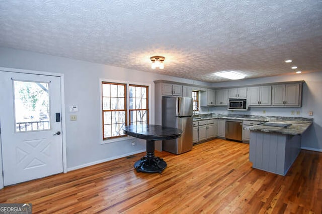 kitchen with a textured ceiling, gray cabinets, stainless steel appliances, and hardwood / wood-style floors