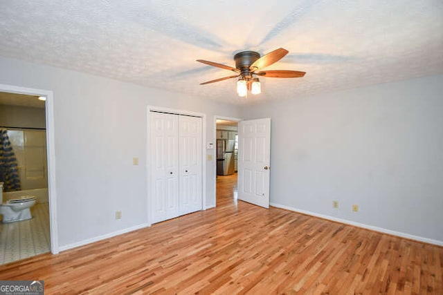 unfurnished bedroom featuring a textured ceiling, ceiling fan, connected bathroom, and stainless steel fridge