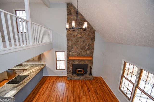 unfurnished living room with a stone fireplace, dark hardwood / wood-style floors, a notable chandelier, high vaulted ceiling, and beamed ceiling