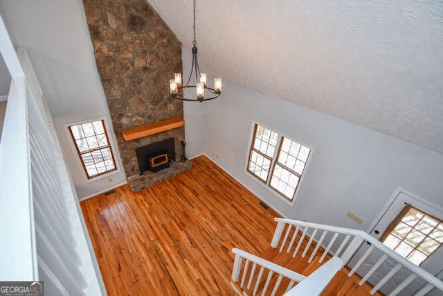 unfurnished living room featuring a notable chandelier, a fireplace, hardwood / wood-style floors, a textured ceiling, and high vaulted ceiling