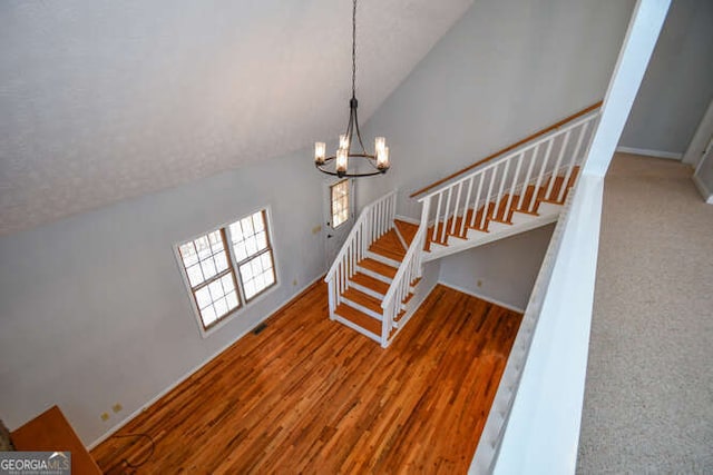 staircase featuring lofted ceiling, wood-type flooring, and a notable chandelier