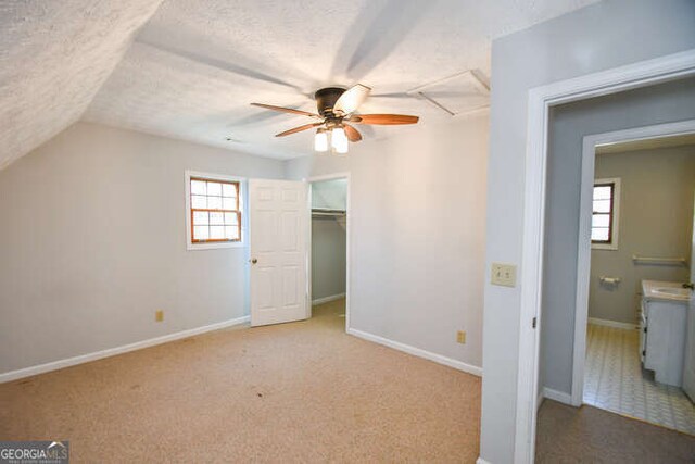 interior space featuring a textured ceiling, ceiling fan, a walk in closet, and light carpet