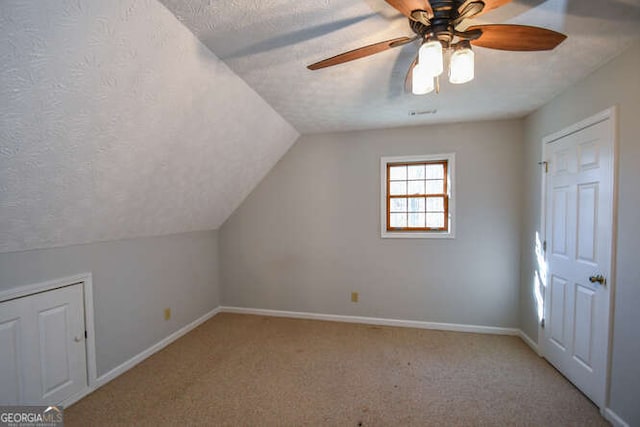 additional living space featuring a textured ceiling, ceiling fan, vaulted ceiling, and light colored carpet