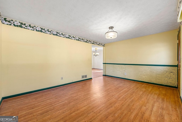 unfurnished room featuring a notable chandelier, a textured ceiling, and light wood-type flooring