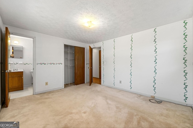 unfurnished bedroom with ensuite bathroom, light colored carpet, and a textured ceiling