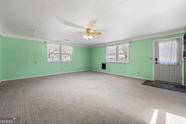 unfurnished living room featuring plenty of natural light, wood walls, ceiling fan, and carpet flooring