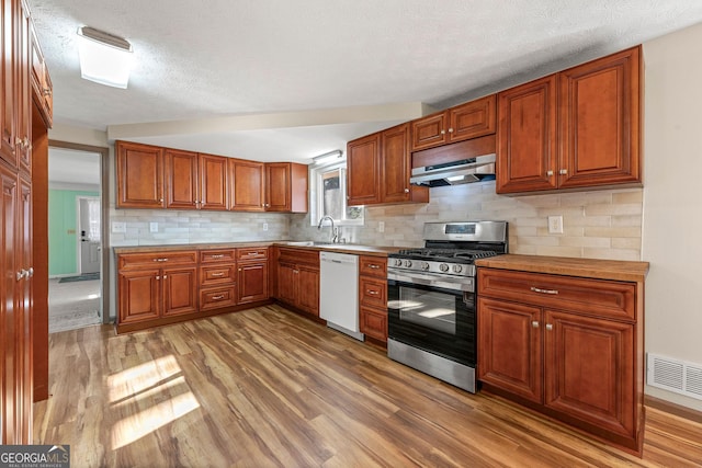 kitchen with sink, dishwasher, stainless steel gas stove, hardwood / wood-style floors, and tasteful backsplash