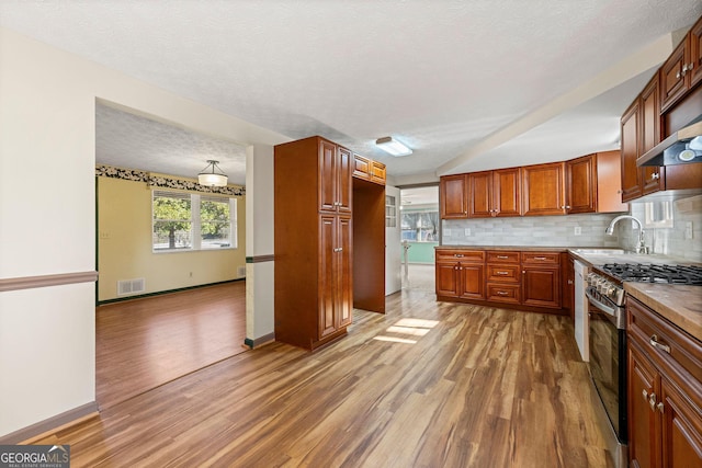 kitchen with sink, backsplash, hardwood / wood-style flooring, gas stove, and a textured ceiling