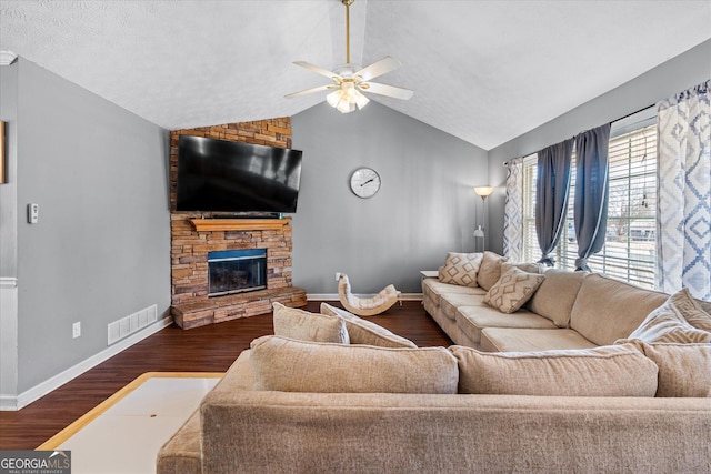 living room featuring ceiling fan, vaulted ceiling, dark wood-type flooring, and a stone fireplace