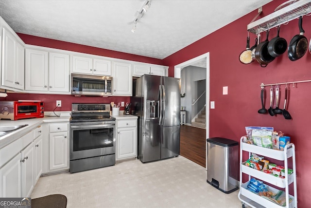 kitchen featuring a textured ceiling, stainless steel appliances, light hardwood / wood-style flooring, and white cabinetry