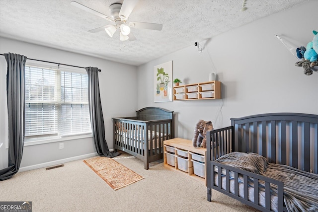 bedroom featuring a textured ceiling, ceiling fan, carpet floors, and a crib