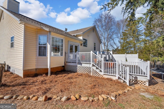 rear view of property with a trampoline and a wooden deck