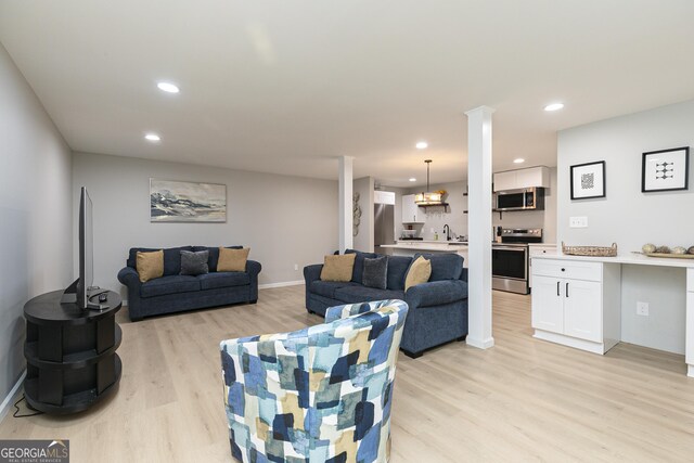 living room with decorative columns, sink, light hardwood / wood-style flooring, and a notable chandelier