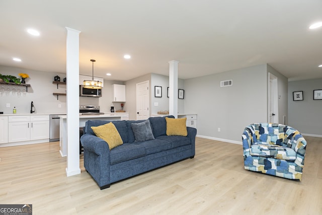 living room with sink, light hardwood / wood-style floors, and decorative columns