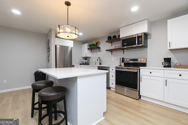 kitchen with appliances with stainless steel finishes, white cabinetry, hanging light fixtures, a center island, and light hardwood / wood-style floors