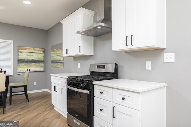 kitchen with white cabinetry, light hardwood / wood-style floors, light stone counters, wall chimney range hood, and stainless steel gas range